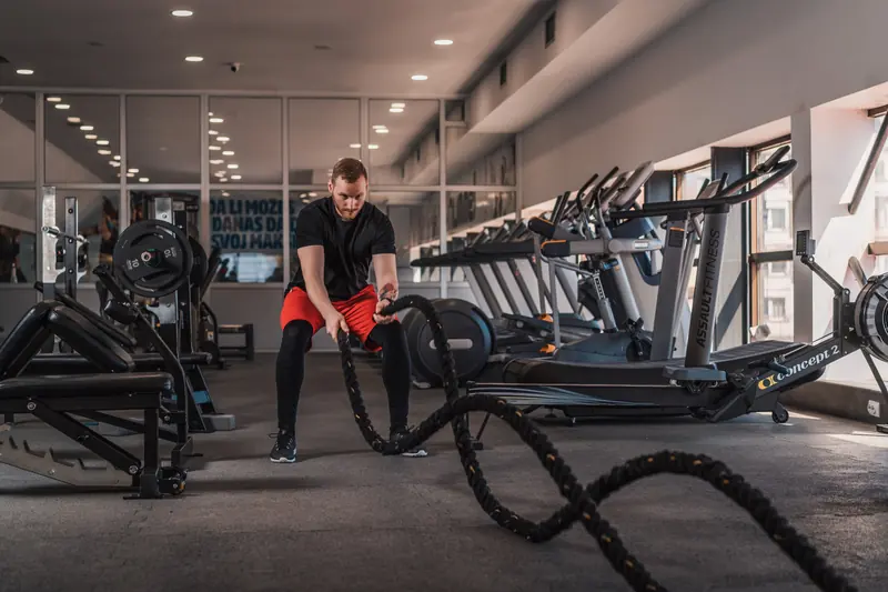 A trainer performing battle-rope exercises in a spacious gym