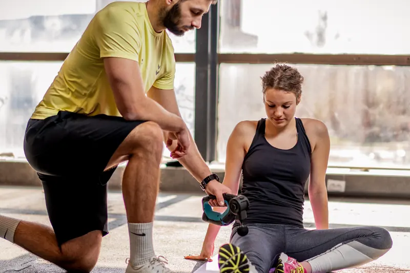 A personal trainer coaching a client through a kneeling exercise on a gym floor